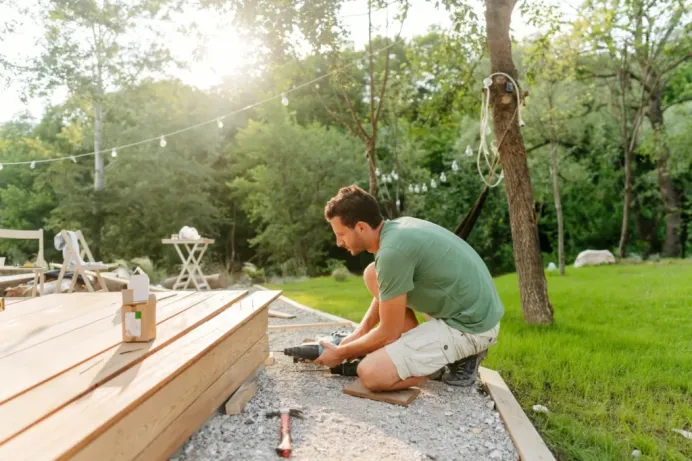 A construction worker kneels while building a deck in a serene backyard, highlighting Bayside Builders Group’s expertise in outdoor remodeling projects in the Bay Area.